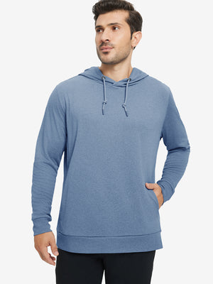 Model with one hand in pocket, wearing classic heather pullover hoodie in colony blue melange, relaxed look.