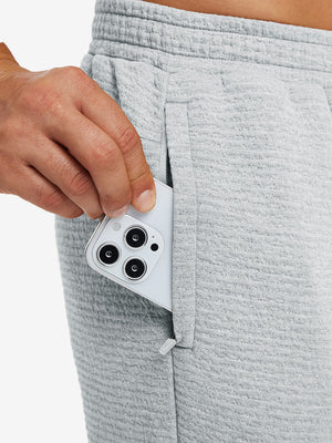 Close-up of iPhone partly inside pocket of light grey heather soft sweatpants with 4 zipper pockets