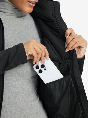 Hand placing an iPhone into pocket of women's lightweight fleece-lined puffer jacket in black.