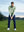 Model on grass under blue sky, leaning on golf club, wearing quarter zip melange pullover in beryl green melange.