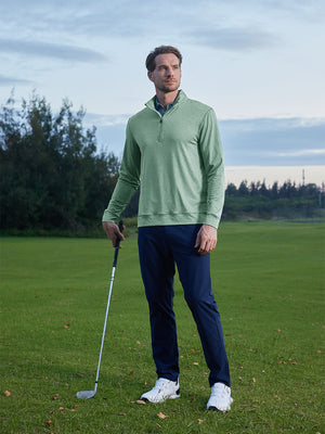 Model on grass under blue sky, leaning on golf club, wearing quarter zip melange pullover in dark green melange.