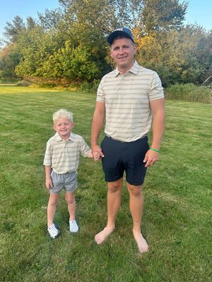 Father holding son's hand outdoors, child wearing kids stylish stripe polo shirts in light khaki stripe