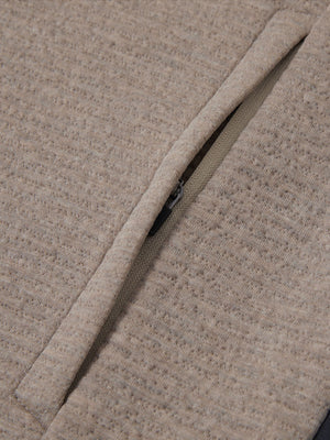 Close-up of jacket pocket showing fine stitching and insulation detail, textured insulated winter jacket, light brown heather.